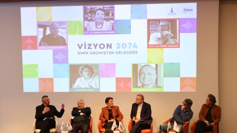 Moderatör ve panelistler sahnede toplu olarak otururken görülüyor